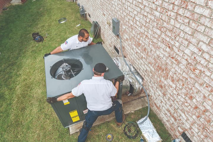 Two HVAC technicians installing a HVAC unit on the side of a house.
